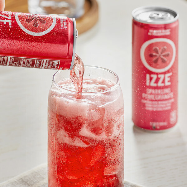A person pouring Izze Pomegranate Sparkling Juice from a red can into a glass with a straw.