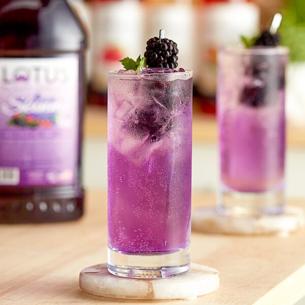 A glass of purple Lotus energy drink with a blackberry on top.