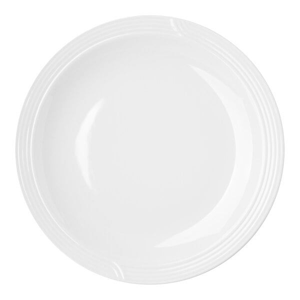 A close-up of a white Dinex china entree plate with a thin curved rim.