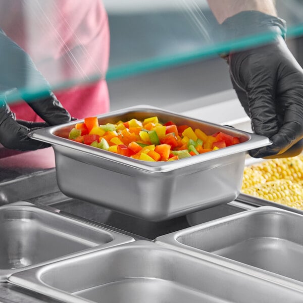A person in gloves holding a Choice stainless steel steam table pan of food.