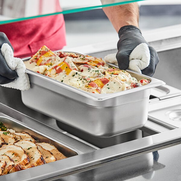 A person in gloves holding a 1/3 size stainless steel pan of food.