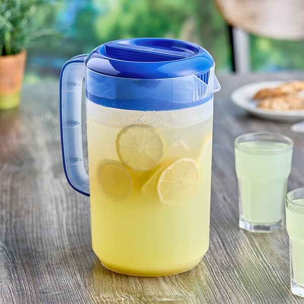 A Choice polypropylene beverage pitcher with blue lid and a glass of lemonade next to it.