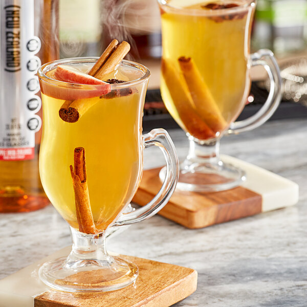 Two glasses of apple cider with cinnamon sticks on a table in a cocktail bar.