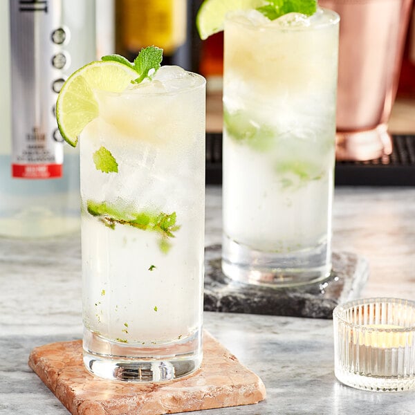 Two glasses of SHOTT Wild Mint drink mix with ice, limes, and mint leaves.