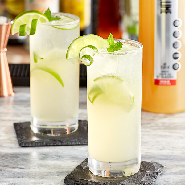 Two glasses of SHOTT Tahitian Lime mixed drinks with lime slices and mint leaves on a marble surface.