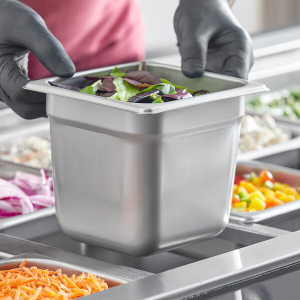 A person in gloves holding a Choice stainless steel steam table pan filled with vegetables.