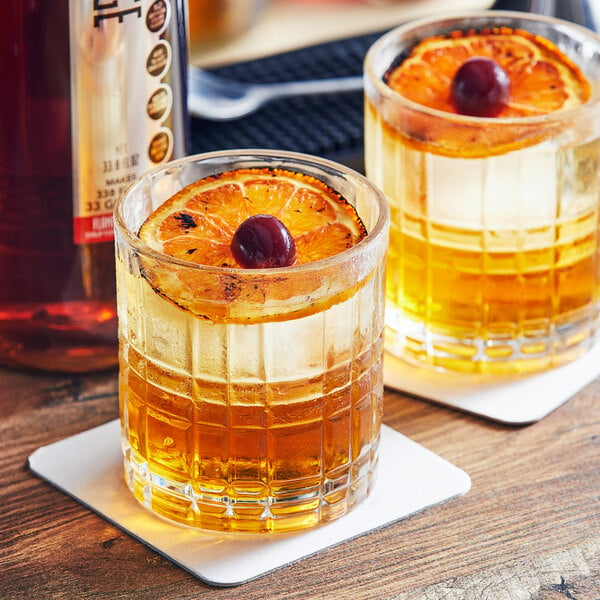 Two glasses of SHOTT Flamed Orange syrup whiskey with orange slices and cherries on a table in a cocktail bar.
