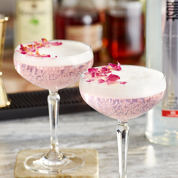 Two glasses of SHOTT rose flavoring syrup with pink liquid and rose petals on top.