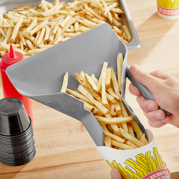 A hand holding a grey-handled plastic scoop of french fries.