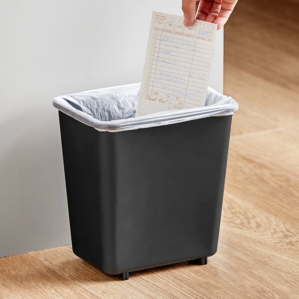A hand putting a receipt in a black Lavex rectangular trash can.