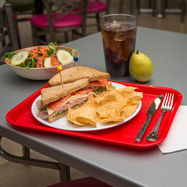 A red Carlisle fast food tray with a sandwich, chips, and a drink on it.