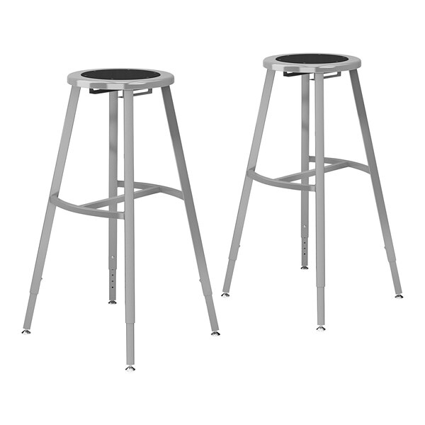 Two National Public Seating gray steel lab stools with black seats and legs.
