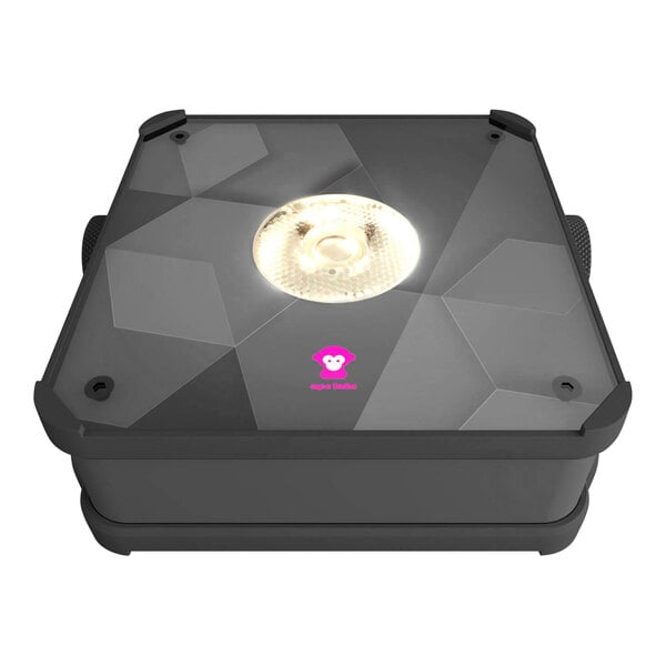 An Ape Labs Mini 2.0 LED light, a black square box with a light on top, lighting a surface outdoors.