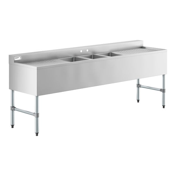 A long stainless steel sink unit with three square basins in the center and drainboards on both ends, supported by four metal legs.