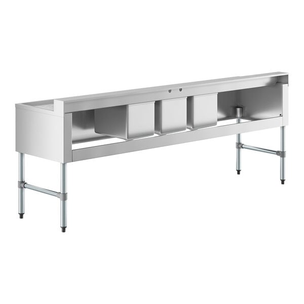 A long, stainless steel sink unit with three square basins and two extended flat drainboards on either side, supported by metal legs.