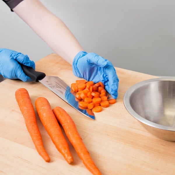 A person in blue gloves using a Mercer Culinary Millennia Chef Knife to cut carrots.