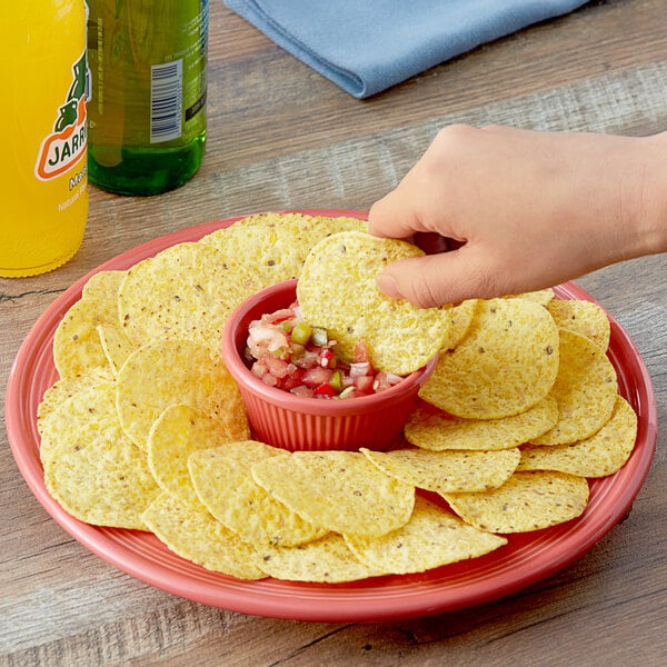 A person holding a Tostitos Thick & Hearty yellow corn chip over a bowl of salsa.