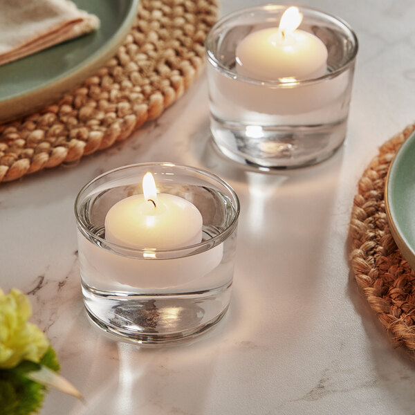 Two Hollowick white wax floating candles in glass cups on a table with green napkins.