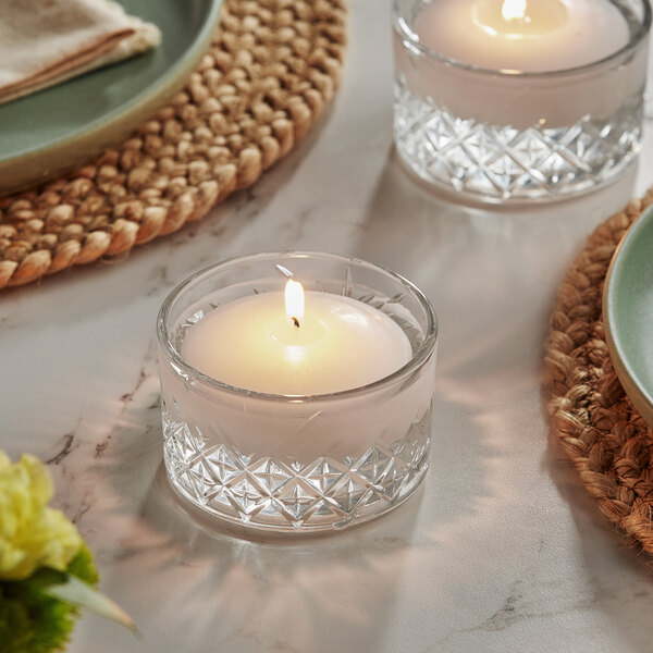A white Hollowick wax floating candle in a glass holder on a table with three small glass votives.