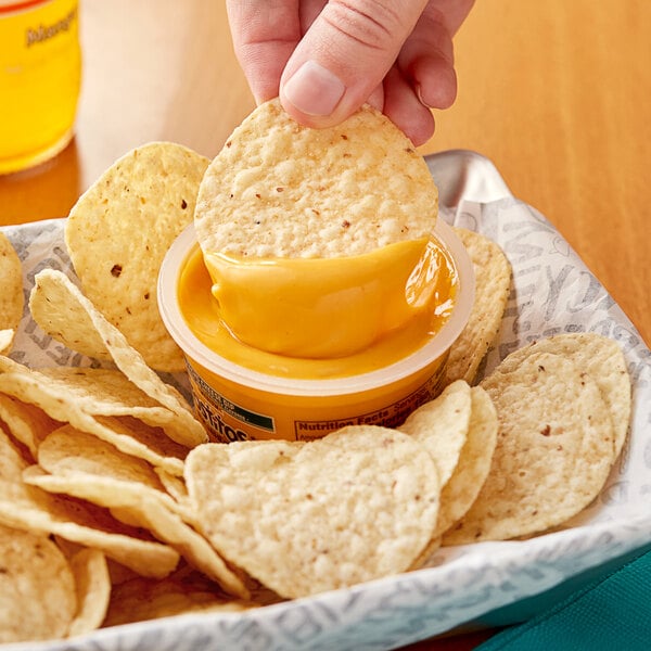 A person dipping a Tostitos Nacho Cheese cup into a bowl of chips.
