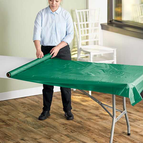 A woman rolling a Hunter Green plastic table cover onto a table.