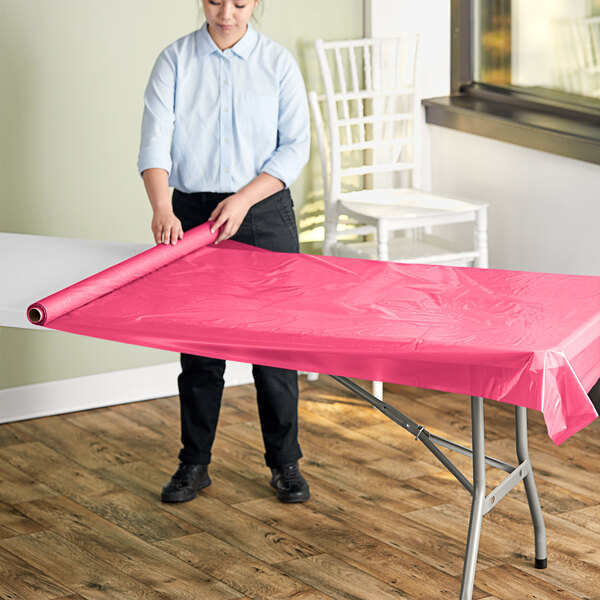 A woman rolling a hot pink plastic table cover