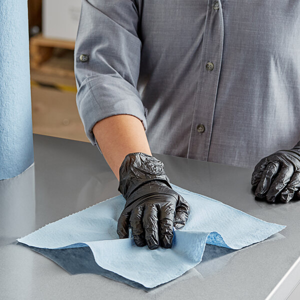 A person wearing black gloves using a Scott Shop Towel to clean a table.