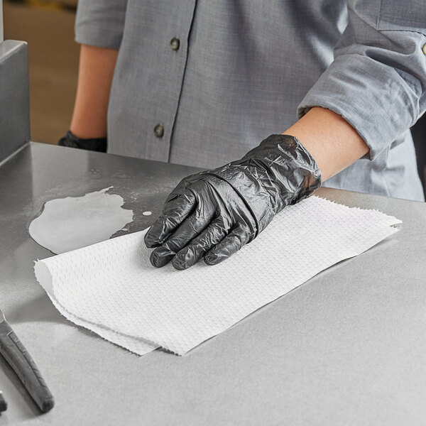 A person wearing black gloves cleaning a counter with a WypAll X80 white wiper.