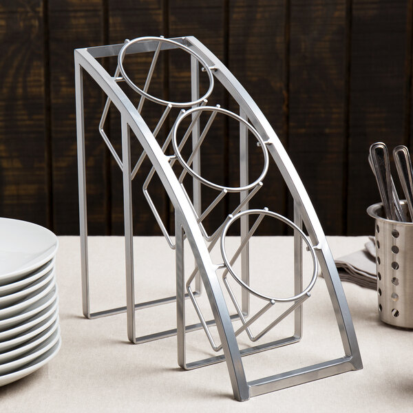 A silver metal Cal-Mil rack with cylindrical holders holding flatware on a table.