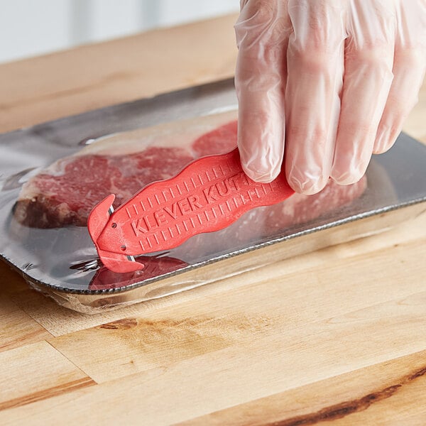 A person using a red Klever Kutter to open a plastic container of red meat.