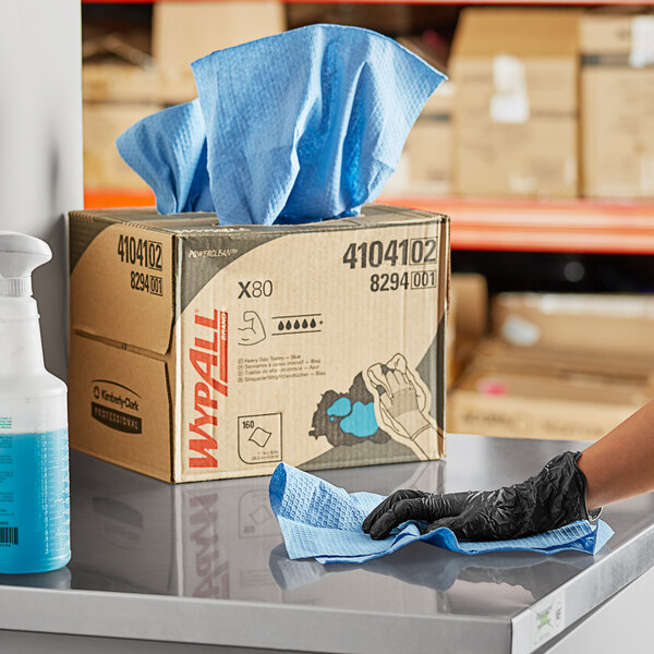 A woman wearing blue gloves cleaning a box with WypAll blue wipers.