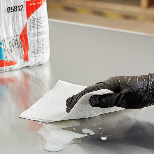 A person in a black glove cleaning a surface with a white WypAll wiper.