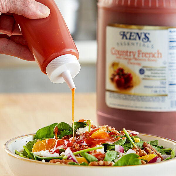 A hand pouring Ken's Country French dressing onto a salad.