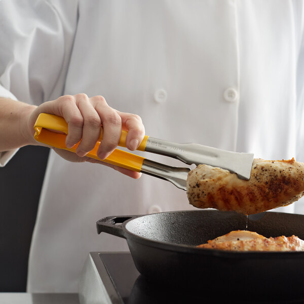 A person using Vollrath VersaGrip tongs to cook chicken in a pan.