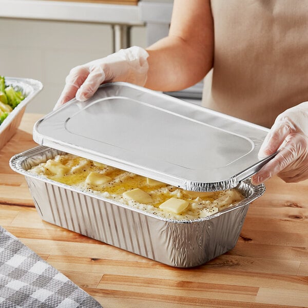 A person holding a Choice 1/3 Size Foil Steam Table Pan with food in it.