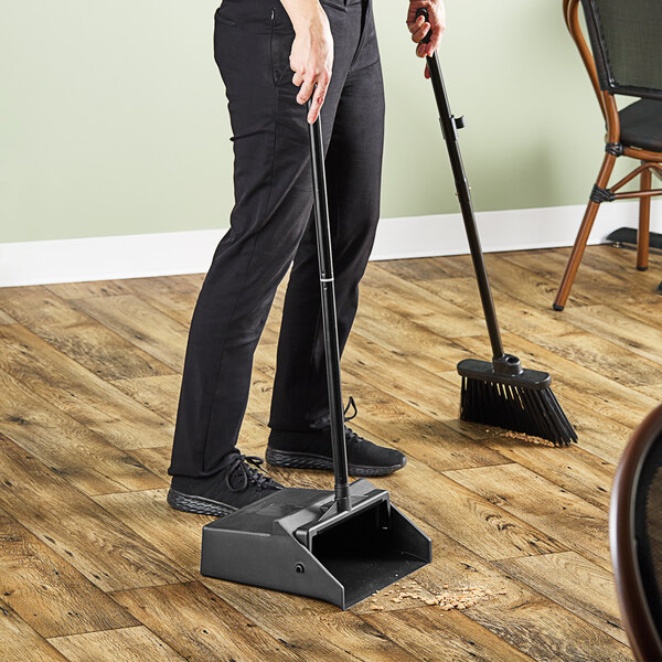 A man using a Carlisle lobby dustpan and broom to sweep the floor in a professional kitchen.