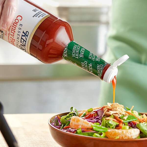 A person pouring Ken's Country French with Orange Blossom Honey Dressing on a bowl of salad.