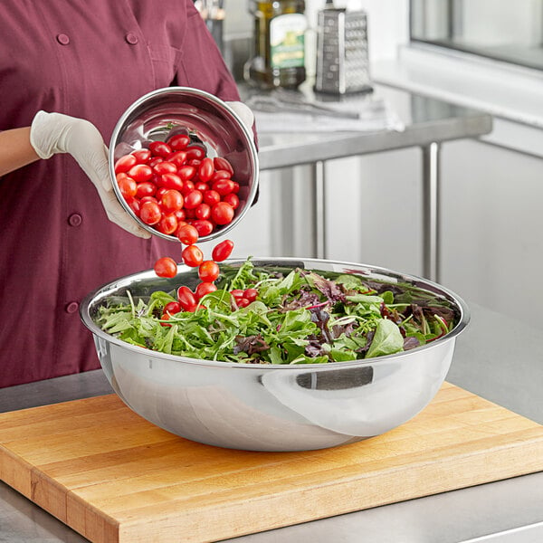 A woman using a Choice heavy weight stainless steel mixing bowl to make a salad with cherry tomatoes.