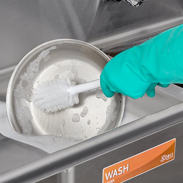 A gloved hand using a Carlisle dish brush to wash a bowl over a sink.