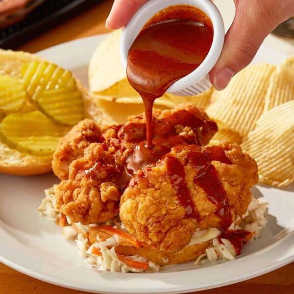 A person pouring Sweet Baby Ray's Nashville Hot Sauce on a plate of food.