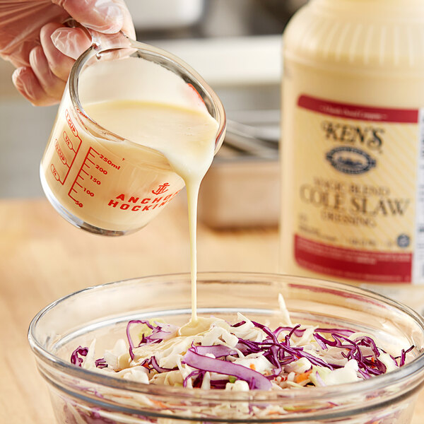 A person pouring Ken's Foods Magic Blend Cole Slaw Dressing into a bowl of coleslaw.