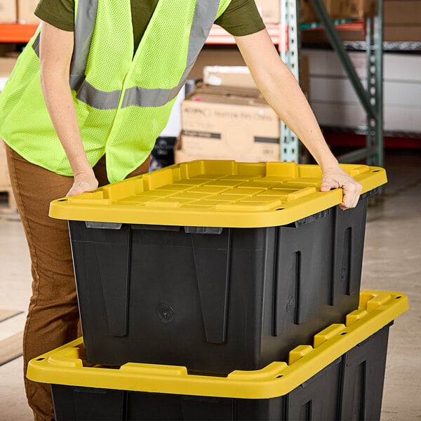 A woman in a safety vest pushing a stack of black Tough Boxes with yellow lids.