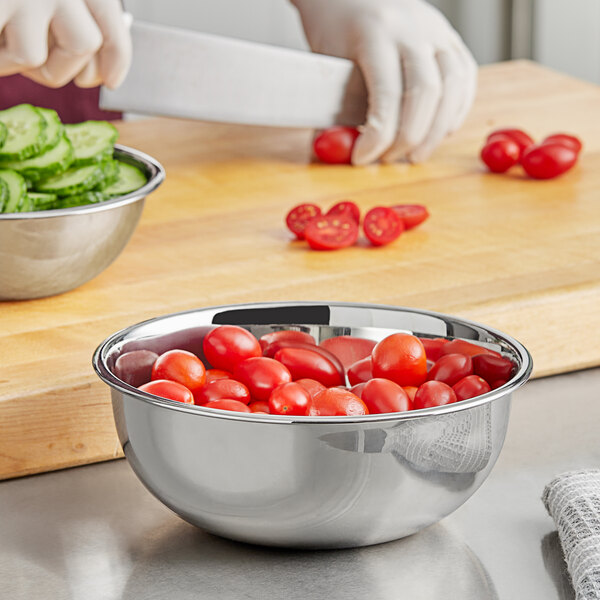A person cutting tomatoes in a Choice stainless steel mixing bowl on a cutting board.