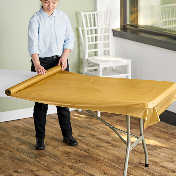 A woman rolling out a metallic gold plastic table cover onto a table.