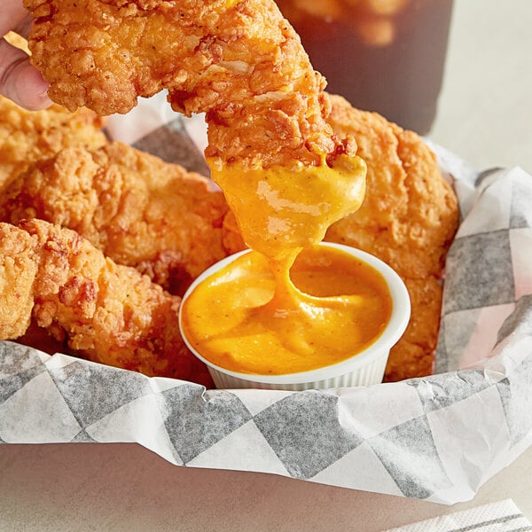 A person dipping Ken's Chick'n Dip'n Sauce into fried chicken.