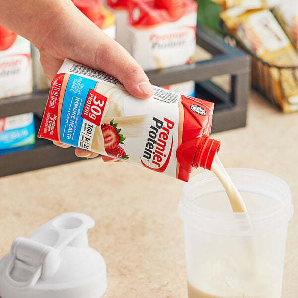 A hand pouring milk into a plastic container of Premier Protein.