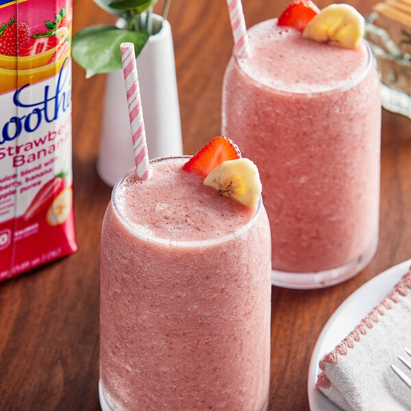 Two glasses of pink Goya strawberry banana smoothies with straws and bananas.