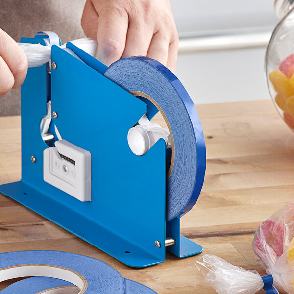 A person using a blue Lavex poly bag sealer tape dispenser to cut tape on a table.