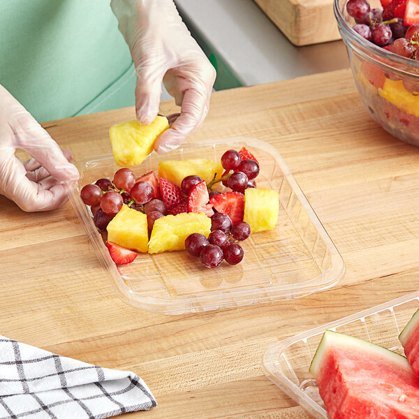 A person in gloves putting pineapple in a clear plastic tray.