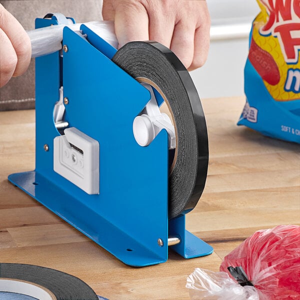 A hand using a blue tape dispenser to cut black Lavex bag sealer tape.